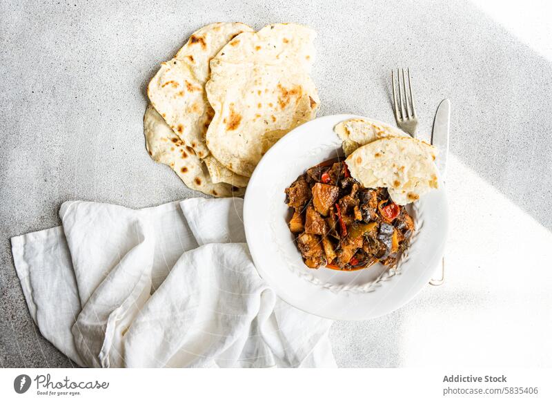 Homemade Vegetable Stew and Flat Bread on White Surface vegetable stew homemade flat bread eggplant tomato potato bell pepper onion garlic basil food cuisine