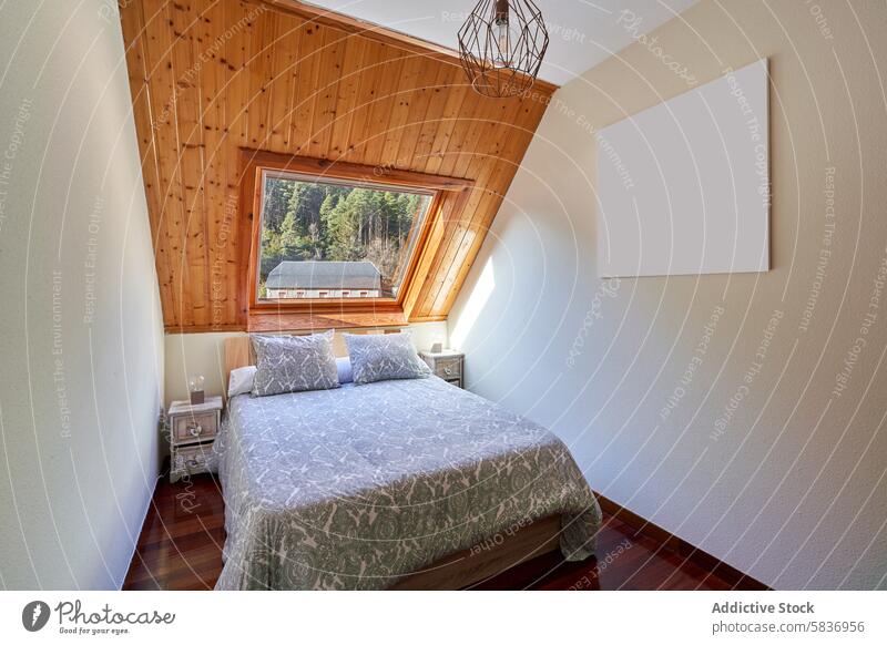 Small bedroom in attic of rural house interior design wooden ceiling forest view skylight window patterned bedspread side table inviting cozy panoramic