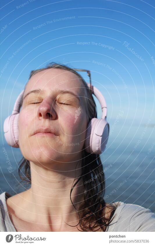 a woman with headphones by the sea. relaxing, unwinding. listening to music, listening to a podcast. Ocean holidays Happiness Caucasian Life Woman Nature