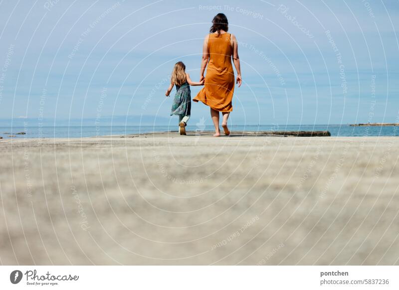 Mother and child walk hand in hand along a concrete footbridge by the sea. Child Love Hold hands Happy Together Family & Relations Feeling of togetherness