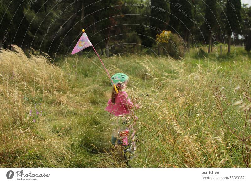 a child on a bicycle with a pennant in the tall grass Child Kiddy bike Girl Pink Bike helmet Trip Cycling tour grasses burdensome Leisure and hobbies Movement