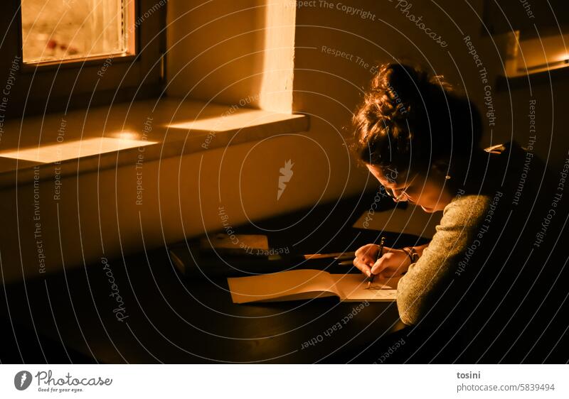 A woman draws through the window at her desk by streetlight Light Window Draw Artist Woman Evening Paper Creativity Leisure and hobbies Interior shot Painter
