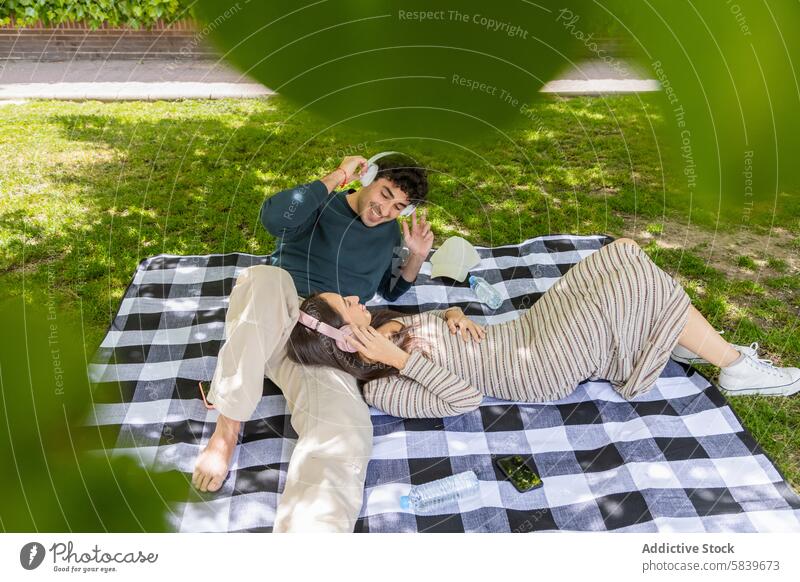 Couple enjoying a relaxed moment on a picnic blanket in the park couple relaxation headphones smile woman green shade leisure outdoor love happy casual