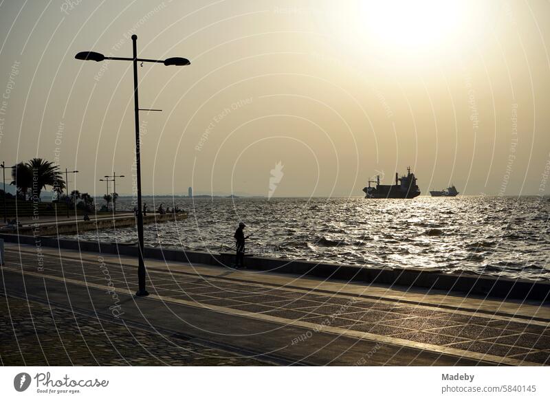 View of the bay of Izmir from the jetty in the Konak district with anglers and anchored ships in the summer from the light of the evening sun on the Aegean Sea in Turkey