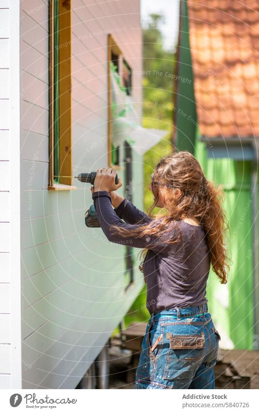 Young Woman Doing Handywork on a Farmhouse woman drilling power tool farmhouse repair maintenance rural farm life handywork diy carpentry outdoor renovation