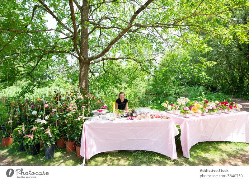 Woman at a sunny farm garden table with plants woman young flower potted plant smile florist rustic outdoor looking at camera countryside nature tree summer