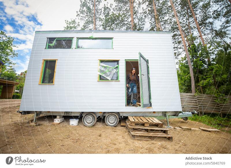 Young woman in a tiny house on a sunny day young wheels rural compact living door trees modern sustainable lifestyle simplicity nature minimalist outdoor