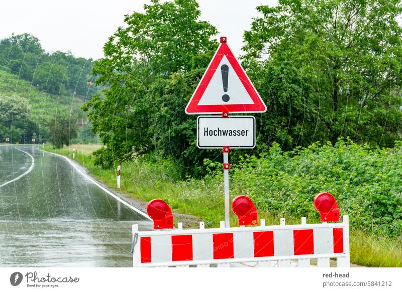 Official road closure due to flooding, with traffic sign, in front of rain-soaked country road, vineyard, trees in the background Flood Rain Country road