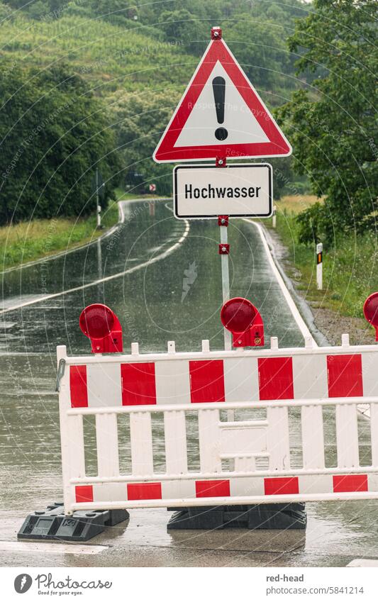 Official road closure due to flooding, with traffic sign, in front of rain-soaked country road, vineyard, trees in the background Flood Rain Country road