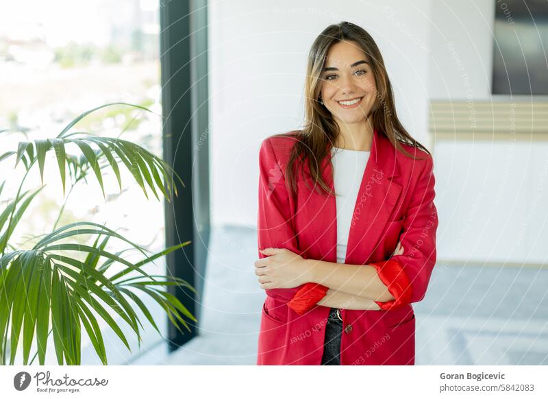 Confident woman smiling in bright office space during daytime smile red blazer confident indoors modern workplace natural light professional business plant