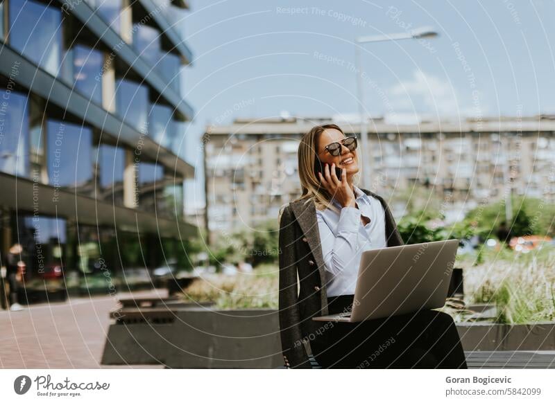 Businesswoman engaged in a call outside a modern office building, midday businesswoman professional workplace laptop smartphone sunny daytime career technology