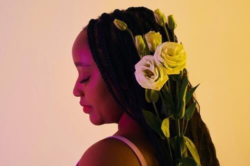 Calm Black woman with white roses in braided hair flower bloom romantic beauty blossom calm jump pink tender present birthday portrait face Love hairstyle light