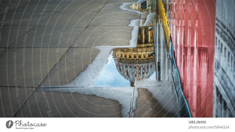 The dome of the cathedral (St. Paul's Cathedral) is reflected in a small puddle on the paving slabs, right next to a postered wall Puddle reflection Church