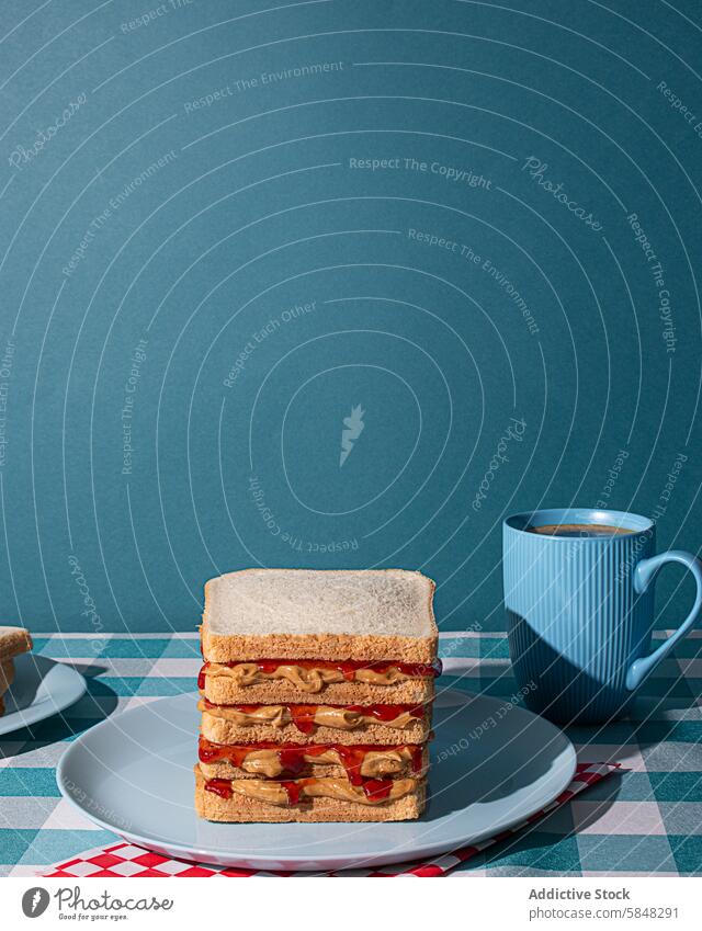 Delicious peanut butter and Jelly sandwiches served on a blue plate , with a cup of an american coffee and some bread slices in a blue background BREAD