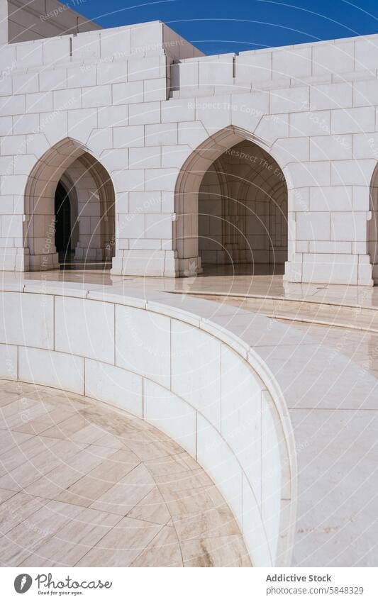 Serene Curved Walkway in Omani Architecture architecture oman walkway curve archway tranquil blue sky clear serene peaceful tradition omani elegant pathway