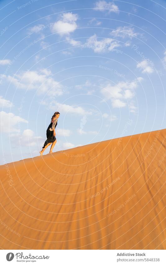 Woman Climbing Sand Dune Under Clear Sky in Oman Desert desert sand dune woman climbing sky clear blue dress scarf bare foot golden sunny outdoor adventure