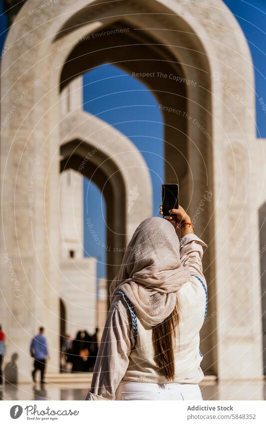 Woman exploring Oman Captures Memories at Architectural Site woman smartphone photo archway architecture travel culture journey modest attire captures essence