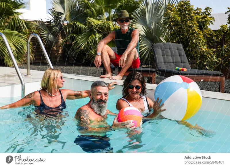 Senior friends enjoying a fun summer day at the pool senior joyful sunlit lush greenery man woman laugh play colorful beach ball active carefree retirement