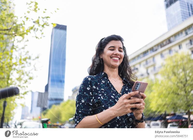 Smiling young woman using her smartphone in the city Indian real people fun summer enjoying street travel outdoors urban adult young adult attractive authentic