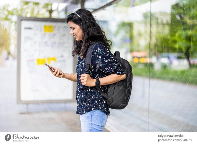 Young woman using smart phone at the bus stop in the city Indian real people fun summer enjoying street travel outdoors urban adult young adult attractive