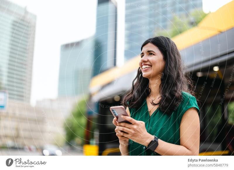 Young woman using smart phone at the bus stop in the city Indian real people fun summer enjoying street travel outdoors urban adult young adult attractive