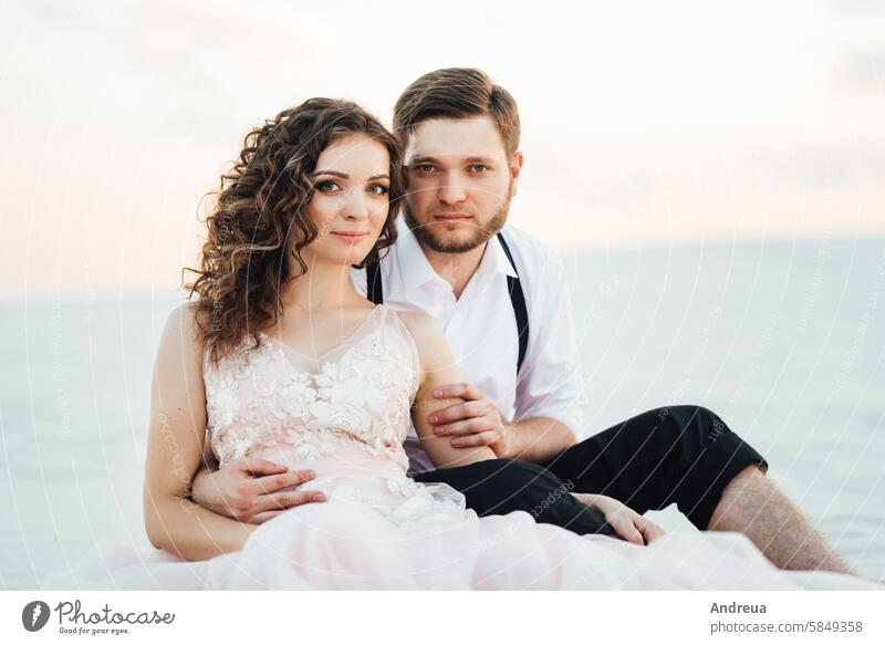 young couple a guy in black breeches and a girl in a pink dress are walking along the white sand barefoot blue day footprints freedom fun on the sand jeans joy