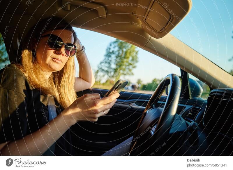 Woman Using Smartphone While Driving in a Car woman smartphone car driving sunglasses driver safety distraction road vehicle afternoon sunny seat device