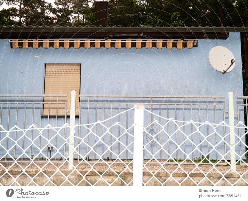 House facade with awning, satellite dish and window, behind two fences Facade Fences Satellite Dish Sun blind Building Blue House (Residential Structure)