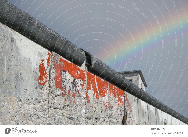 Section of the wall runs diagonally, part of the upper floor of a building protrudes in the background, a colorful rainbow from west to east connects like a bridge