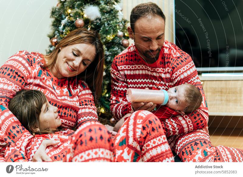 Cozy family moment during Christmas celebration christmas festive pajamas father mother baby feeding bottle affection bonding tree holiday home cozy matching