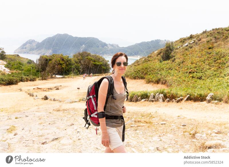 Hiker enjoying a summer coastal landscape woman hiker backpack smile coastal trail nature sea view outdoors travel adventure leisure sunny trek recreation ocean