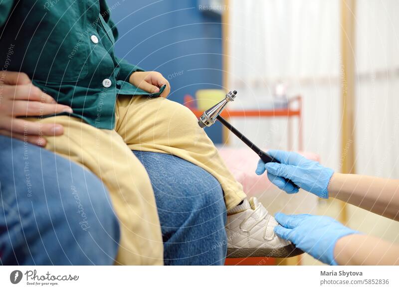 Baby and his mother are being seen by a pediatric neurologist in a modern medical clinic. Doctor conducts tests, checks the reflexes using neurological hammer of small patient. Highly qualified cure