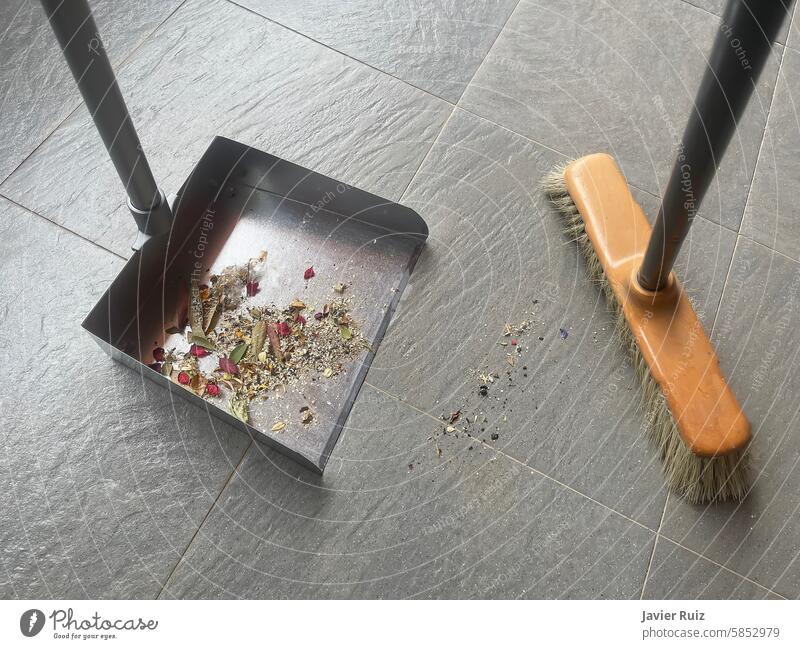 first person view of a wooden broom and a metal dustpan with some of the uncollected rubbish on a grey tile floor sweeper brush tiled waste sweeping top view