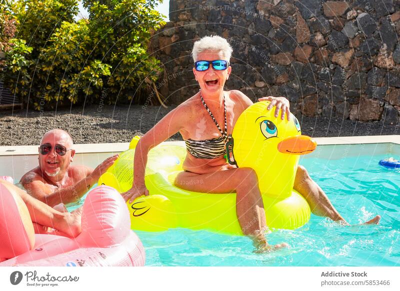 Joyful seniors enjoying a sunny day in the pool swimming pool inflatable toy duck float couple water fun summer outdoor leisure activity elderly smile happy