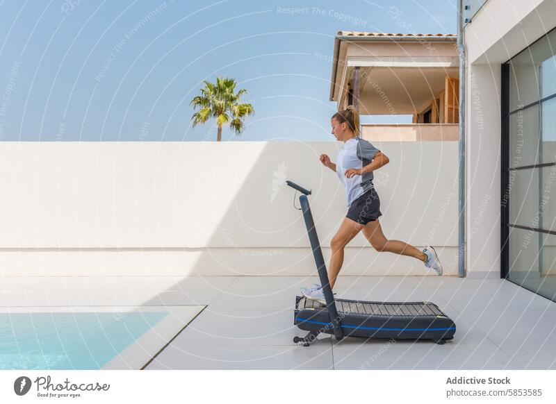 Young woman exercising on treadmill in outdoor setting exercise fitness athlete running pool sky sunny tropical palm tree modern health wellness active