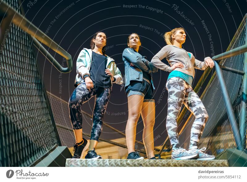 Three women standing on urban stairs at night ready for an evening exercise session in the city female athlete woman runner three staircase step friends group