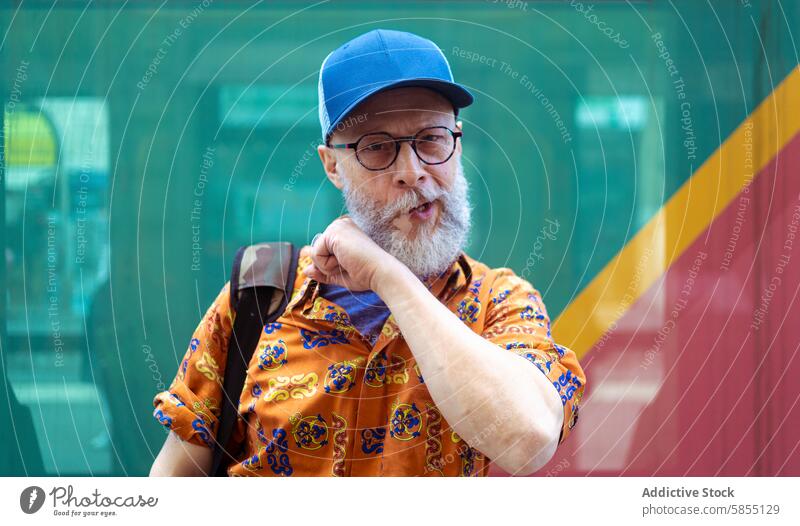 Senior man in stylish attire pondering outdoors senior modern remote work lifestyle thinking colorful shirt cap glasses beard mature contemporary active retiree