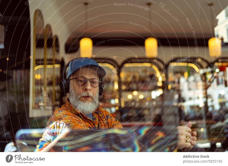 Stylish senior working remotely in a café man remote work stylish laptop headphones modern fashionable colorful shirt cap lifestyle technology entrepreneur