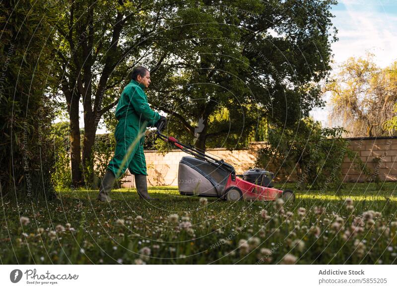 Man mowing a lush garden lawn at sunset man jumpsuit serene landscape trees wildflower tranquil outdoor nature backyard gardening caretaker work equipment