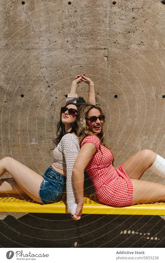 Playful friends enjoying a sunny day at the park woman summer fun cheerful sunglasses dress denim young female bench yellow outdoor casual fashion style