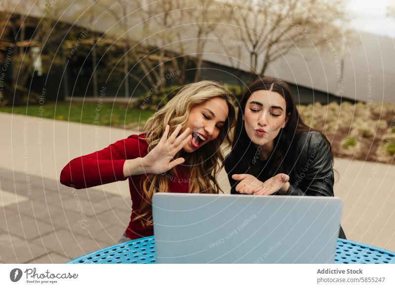 Two friends sending kisses during a video call at the park laptop wave blow kiss playful cheerful young woman outdoor technology connectivity smile happy