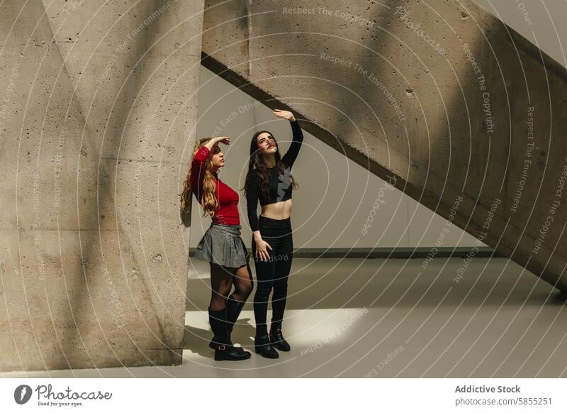 Two young women exploring architectural shadows woman friend architecture exploration portrait interaction pointing female concrete structure urban fashion