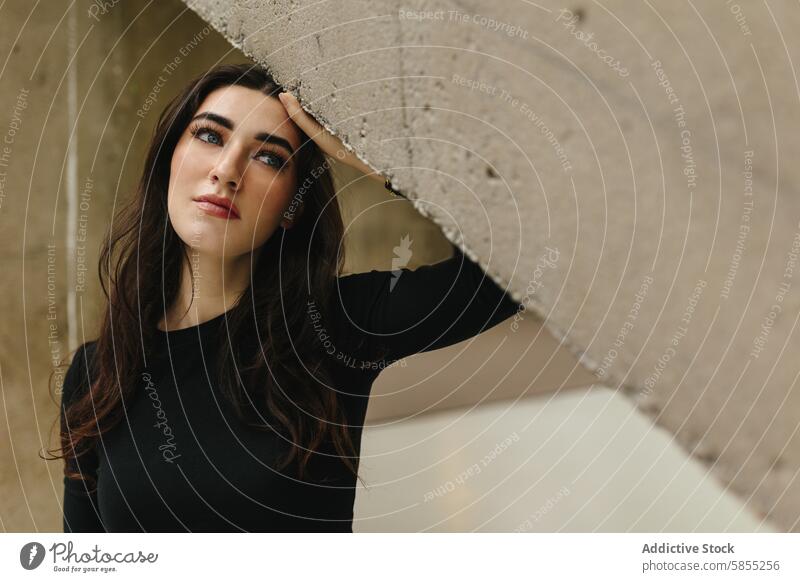 Woman leaning under concrete structure with intense gaze woman portrait makeup beauty young urban architecture texture mood detail eyes expression contemplative