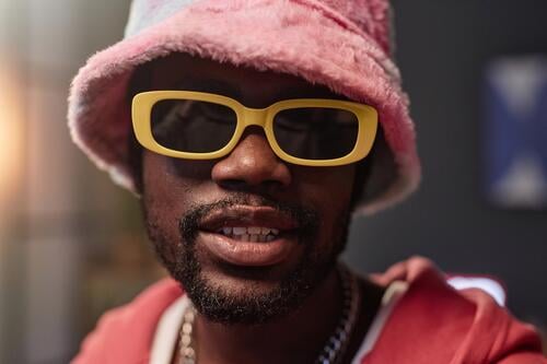 Black Man Wearing Retro Sunglasses and Pink Outfit Black man pink hip-hop sunglasses rapper look at camera record video bucket hat influencer performer