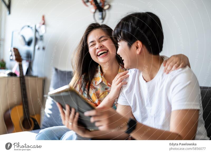 Happy young couple using digital tablet together on the sofa at home asian real people fun enjoying young adult authentic cheerful confident female happy