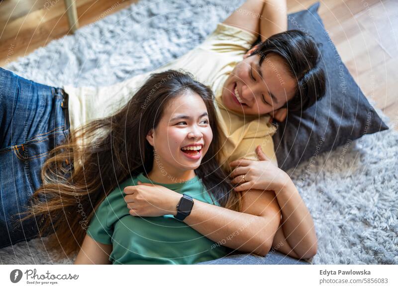 Happy young couple lying on carpet on the floor asian real people fun enjoying young adult authentic cheerful confident female happy millennials natural