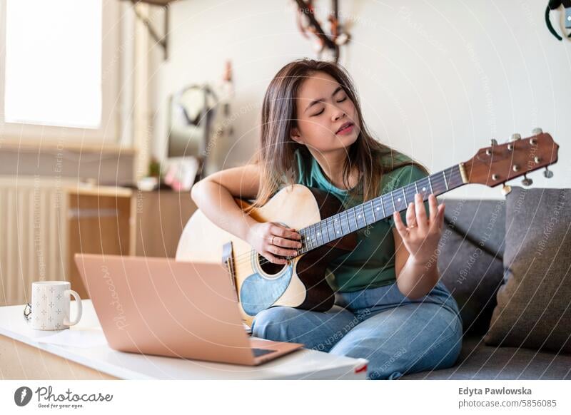 Young woman playing guitar at home asian real people fun enjoying young adult authentic cheerful confident female happy millennials natural portrait positive