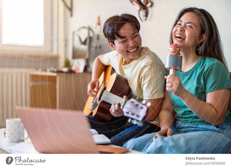 Happy young couple singing and playing the guitar at home asian real people fun enjoying young adult authentic cheerful confident female happy millennials