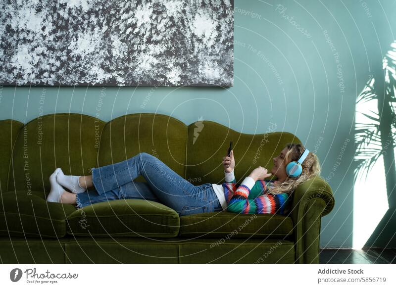 Relaxed individual surfing the web on a couch at home sofa smartphone relaxed leisure abstract artwork green digital technology casual comfort peaceful interior