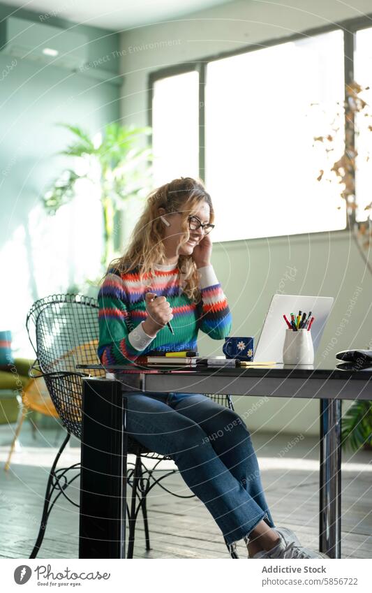 Young woman smiling during a remote work session at home home office laptop young glasses colorful sweater desk conversation technology wireless joy happiness
